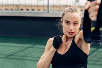 Young woman doing exercises on a rooftop. Fitness female working out outdoors using suspension...