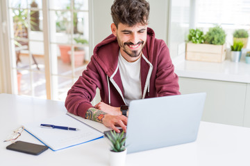 Fototapeta premium Young student man using computer laptop and notebook with a happy face standing and smiling with a confident smile showing teeth