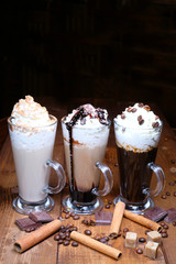 three glass coffee, americano, cappuccino, latte. Great tasty foam. coffee beans, cinnamon scattered on a wooden table