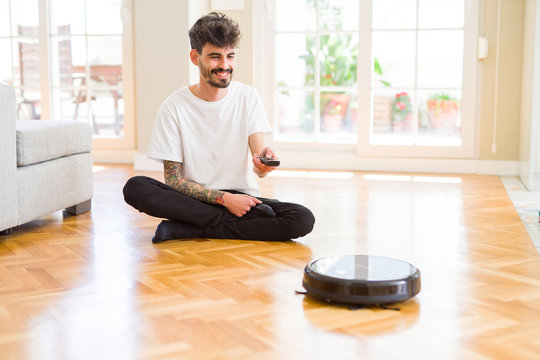 Young man using automatic vacuum cleaner to clean the floor, controling machine housework robot