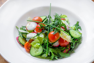 large plate with various kinds of tropical fruit flowers. Food for vegetarians, vegans and raw foodists. On a white plate - salad, arugula, apple, cucumber, radish, onion, tomato. macro