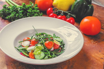 large plate with various kinds of tropical fruit flowers. Food for vegetarians, vegans and raw foodists. On a white plate - salad, arugula, apple, cucumber, radish, onion, tomato. Side view