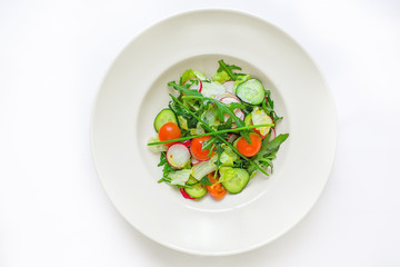 large plate with various kinds of tropical fruit flowers. Food for vegetarians, vegans and raw foodists. On a white plate - salad, arugula, apple, cucumber, radish, onion, tomato. View from above