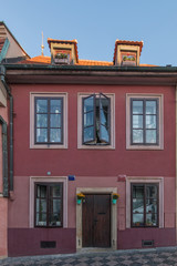 historic two-storey house with window and wooden entrance door near the Petrite tower. Open window with flowers and skylight. Red and brown paint on the brickwork in the evening