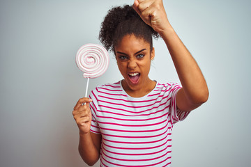 African american teenager woman eating colorful candy over isolated white background annoyed and frustrated shouting with anger, crazy and yelling with raised hand, anger concept