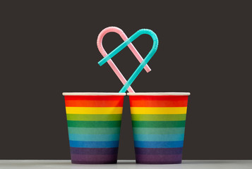 Together forever. Two LGBT color paper cups with pink and blue heart shaped cocktail tubes. The concept of love of people of homosexuality or a symbol of the anniversary of living together. Isolate