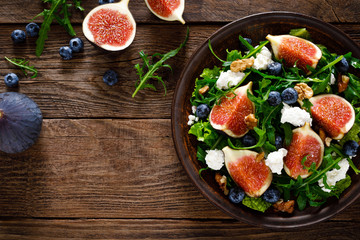 Fig salad with goat cheese, blueberry, walnuts and arugula on wooden background. Healthy food. Top...