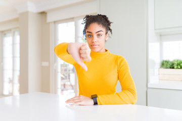 Beautiful african american woman with afro hair wearing a casual yellow sweater looking unhappy and angry showing rejection and negative with thumbs down gesture. Bad expression.
