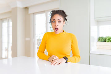 Beautiful african american woman with afro hair wearing a casual yellow sweater In shock face, looking skeptical and sarcastic, surprised with open mouth