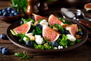 Fig salad with goat cheese, blueberry, walnuts and arugula on wooden background. Healthy food. Lunch