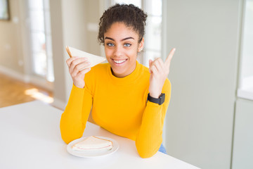 Young african american woman eating a sandwich as healthy snack very happy pointing with hand and finger to the side