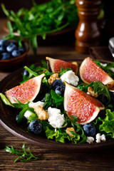 Fig salad with goat cheese, blueberry, walnuts and arugula on wooden background. Healthy food. Lunch