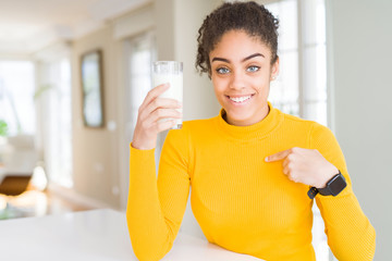 Young african american woman drinking a glass of fresh milk with surprise face pointing finger to himself