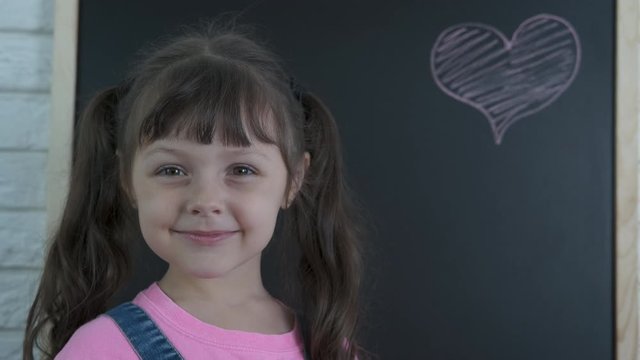 Kid draw a heart. Little girl with a drawn heart on a school board.