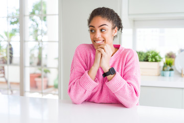 Fototapeta na wymiar Beautiful african american woman with afro hair wearing casual pink sweater laughing nervous and excited with hands on chin looking to the side