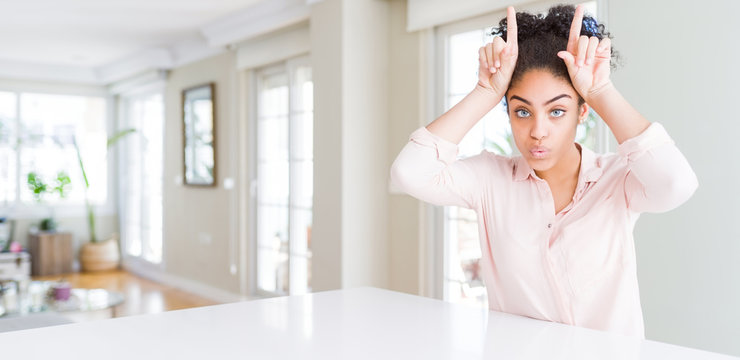 Wide angle of beautiful african american woman with afro hair doing funny gesture with finger over head as bull horns