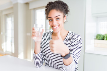 Young african american girl drinking a fresh glass of water happy with big smile doing ok sign, thumb up with fingers, excellent sign