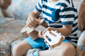  Caucasian child playing and making music chords with small guitar or ukulele, close up