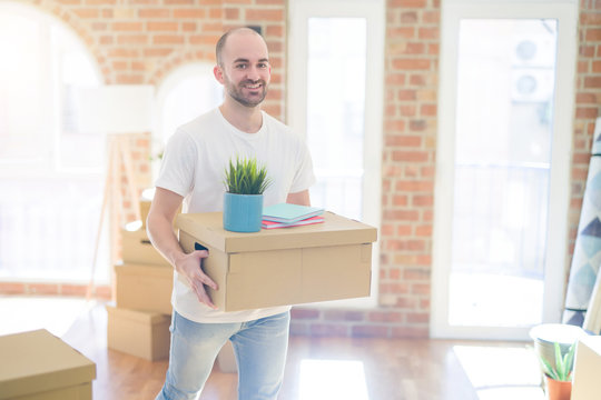 Young handsome man moving to a new house, holding cardboxes smiling very happy for new apartment