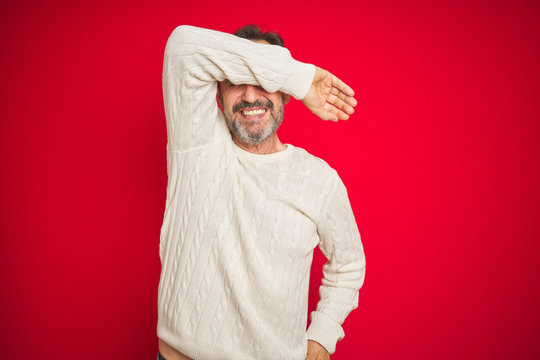 Handsome middle age senior man with grey hair over isolated red background covering eyes with arm smiling cheerful and funny. Blind concept.
