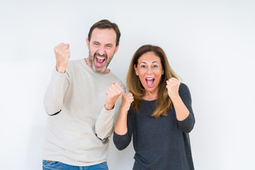 Beautiful middle age couple in love over isolated background very happy and excited doing winner gesture with arms raised, smiling and screaming for success. Celebration concept.