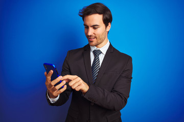 Young handsome businessman using smartphone standing over isolated blue background with a happy face standing and smiling with a confident smile showing teeth
