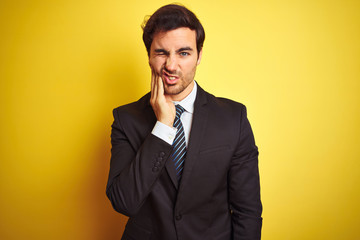 Young handsome businessman wearing suit and tie standing over isolated yellow background touching mouth with hand with painful expression because of toothache or dental illness on teeth. 