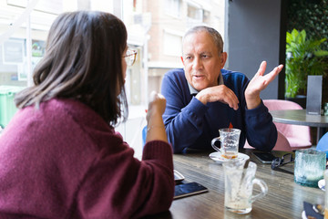 Senior man having a conversation with woman drinking coffee and relaxing, chatting at restaurant