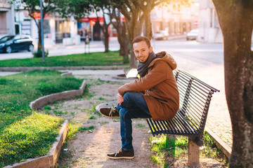 brunette with beard in stylish clothes sits on a bench. evening