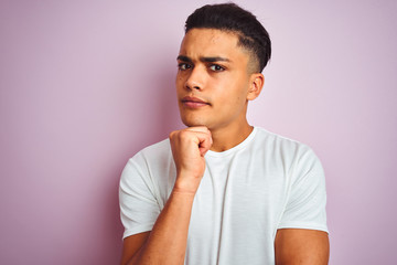 Young brazilian man wearing t-shirt standing over isolated pink background serious face thinking about question, very confused idea