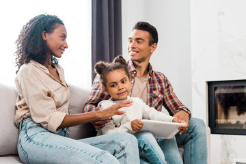 kid holding digital tablet while african american parents looking at each other