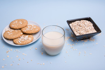 Leche de avena vegana sobre una mesa en un vaso de cristal, un bol con copos de avena y un plato de galletas.