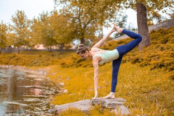 beautiful sporty girl standing in Half Moon pose, Ardha Chandrasana exercise Slender. yoga exercises on the green grass in autumn against the background of nature