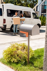 Fototapeta na wymiar selective focus of mailbox and african american couple holding boxes while standing near car