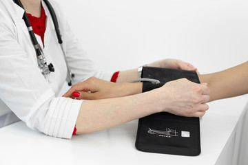 Professional female doctor putting on device for measuring pressure on young female patient hand in hospital room