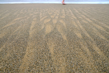 Feet of a walking person, wet sand on beachin flat shadeless light.