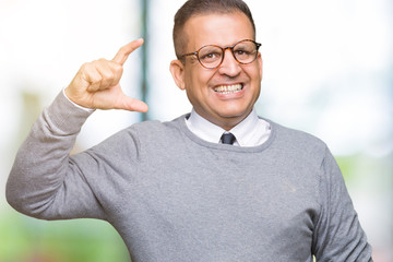 Middle age bussines arab man wearing glasses over isolated background smiling and confident gesturing with hand doing size sign with fingers while looking and the camera. Measure concept.