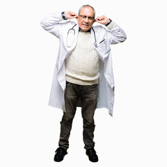 Handsome senior doctor man wearing medical coat Smiling pulling ears with fingers, funny gesture. Audition problem