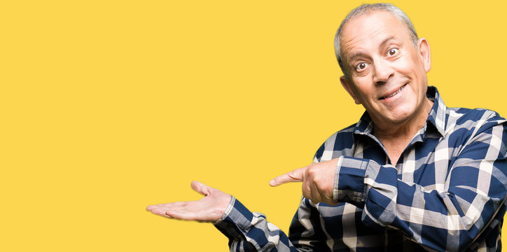 Handsome senior man wearing casual shirt amazed and smiling to the camera while presenting with hand and pointing with finger.