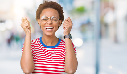 Beautiful young african american woman wearing glasses over isolated background excited for success with arms raised celebrating victory smiling. Winner concept.