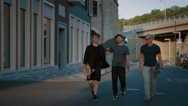 Three Cool Guys Talking, Having Fun while Walking and Carrying Skateboards. Stylish Young Friends Strolling down the Street. In the Background Fashionable Modern Hipster District