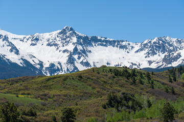 Low angle landscape of green hillside and snow-covered mountains behind at the Dallas Divide in...