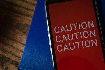 smartphone displaying generic application (app) with information CAUTION in screen, on table with dramatic lighting