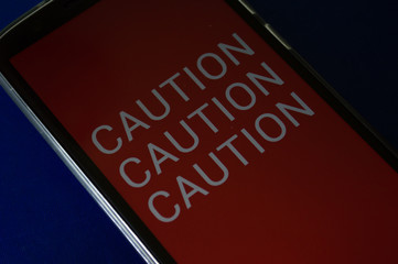 smartphone displaying generic application (app) with information CAUTION in screen, on table with...