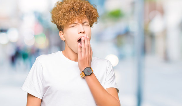 Young handsome man with afro hair wearing casual white t-shirt bored yawning tired covering mouth with hand. Restless and sleepiness.