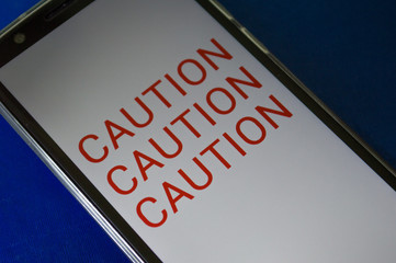 smartphone displaying generic application (app) with information CAUTION in screen, on table with...