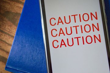 smartphone displaying generic application (app) with information CAUTION in screen, on table with...