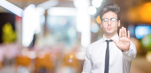 Young business man wearing glasses over isolated background doing stop sing with palm of the hand. Warning expression with negative and serious gesture on the face.