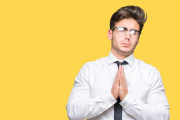 Young business man wearing glasses over isolated background begging and praying with hands together...