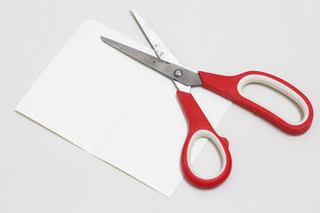 Red scissors on white sheet paper background